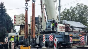 Dźwig Terex Demag z dużym balastem podczas pracy na ciasnym terenie wśród zabudowy jednorodzinnej.