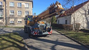 Żuraw Krupp KMK 2020 manewruje na wąskiej ulicy, pomiędzy zabytkowymi kamienicami.