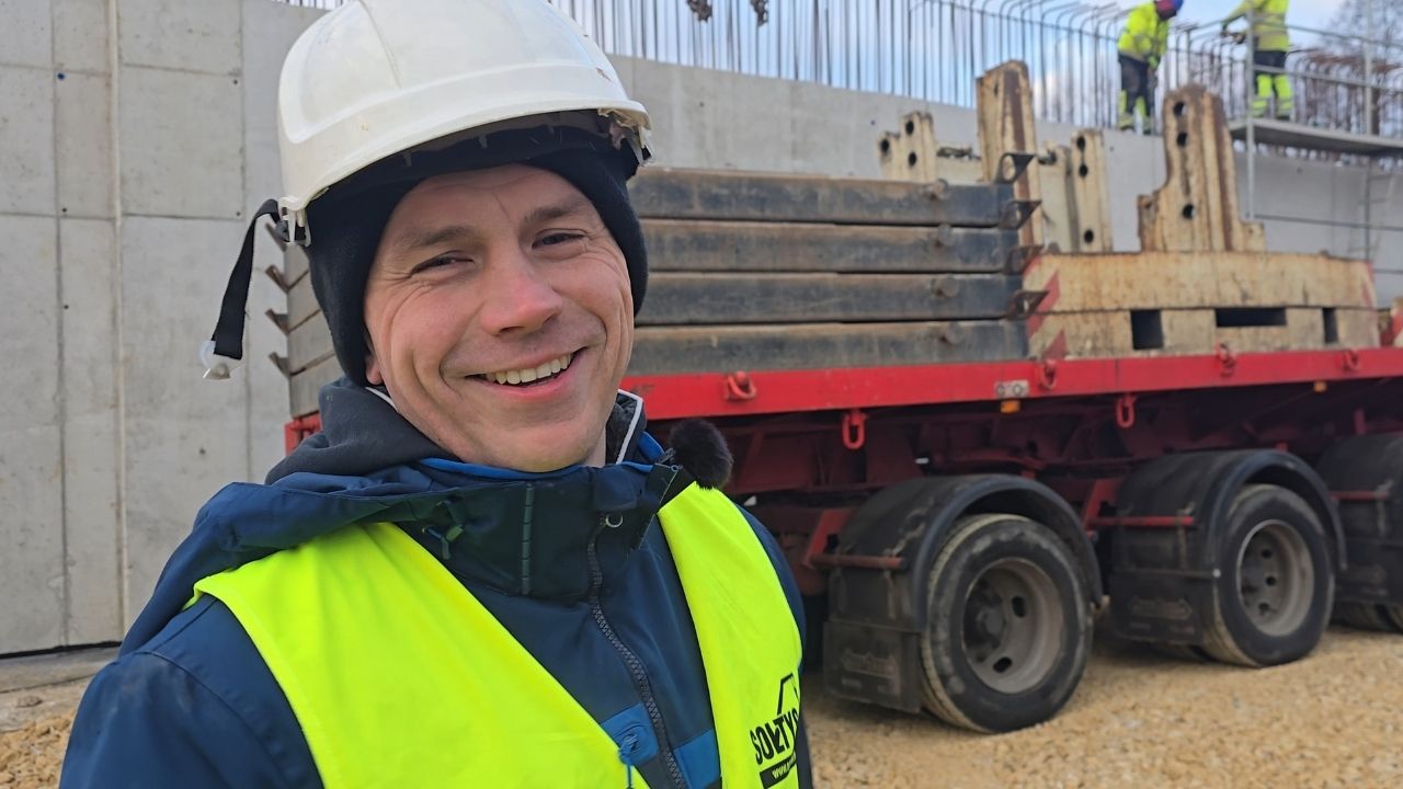 Aleksander Sołtys na tle maszyny transportowej z balastami. 