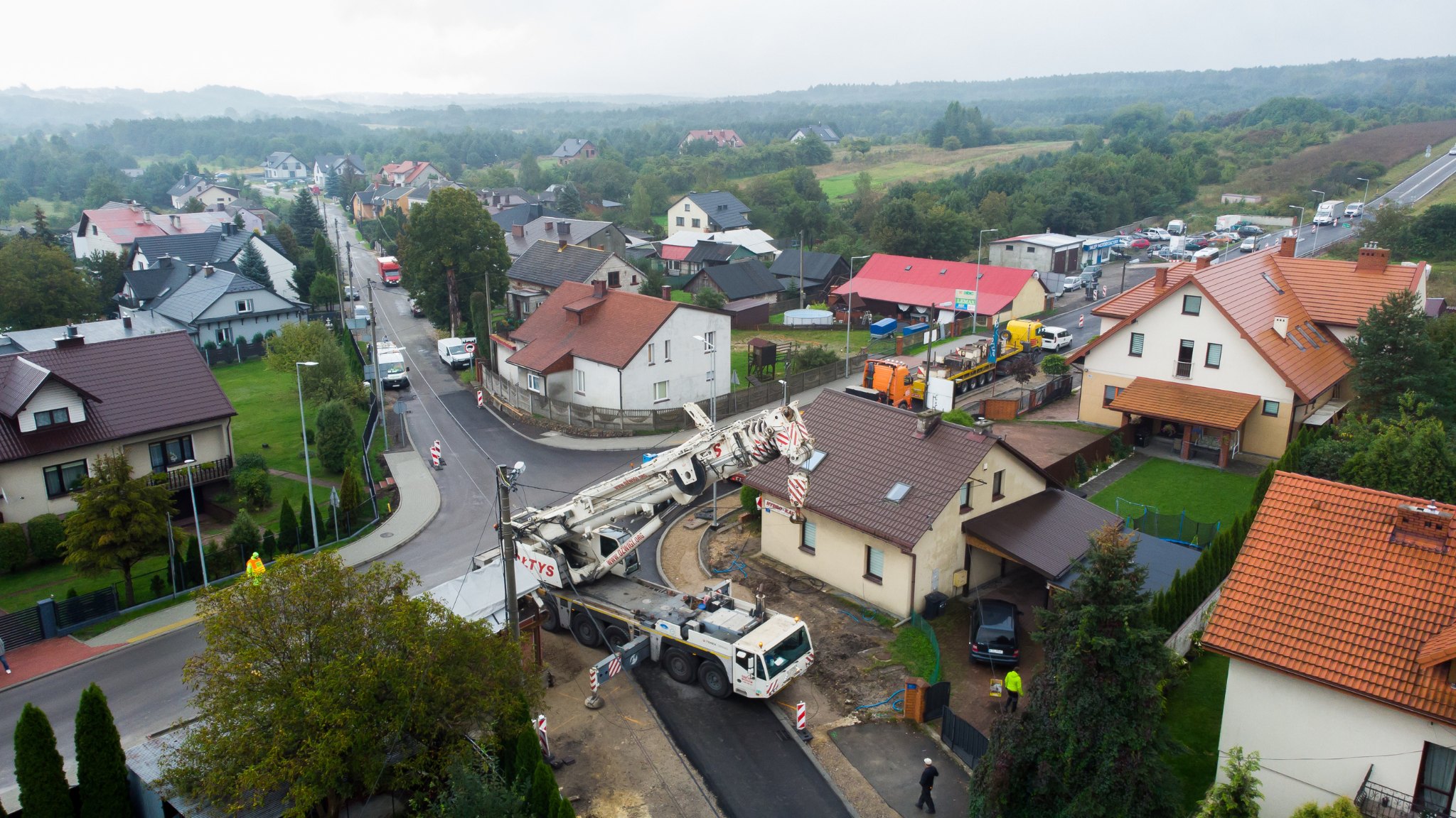 Dźwig samojezdny 350 ton wjeżdża w wąską ulicę pomiędzy domami jednorodzinnymi w centrum małego miasta.