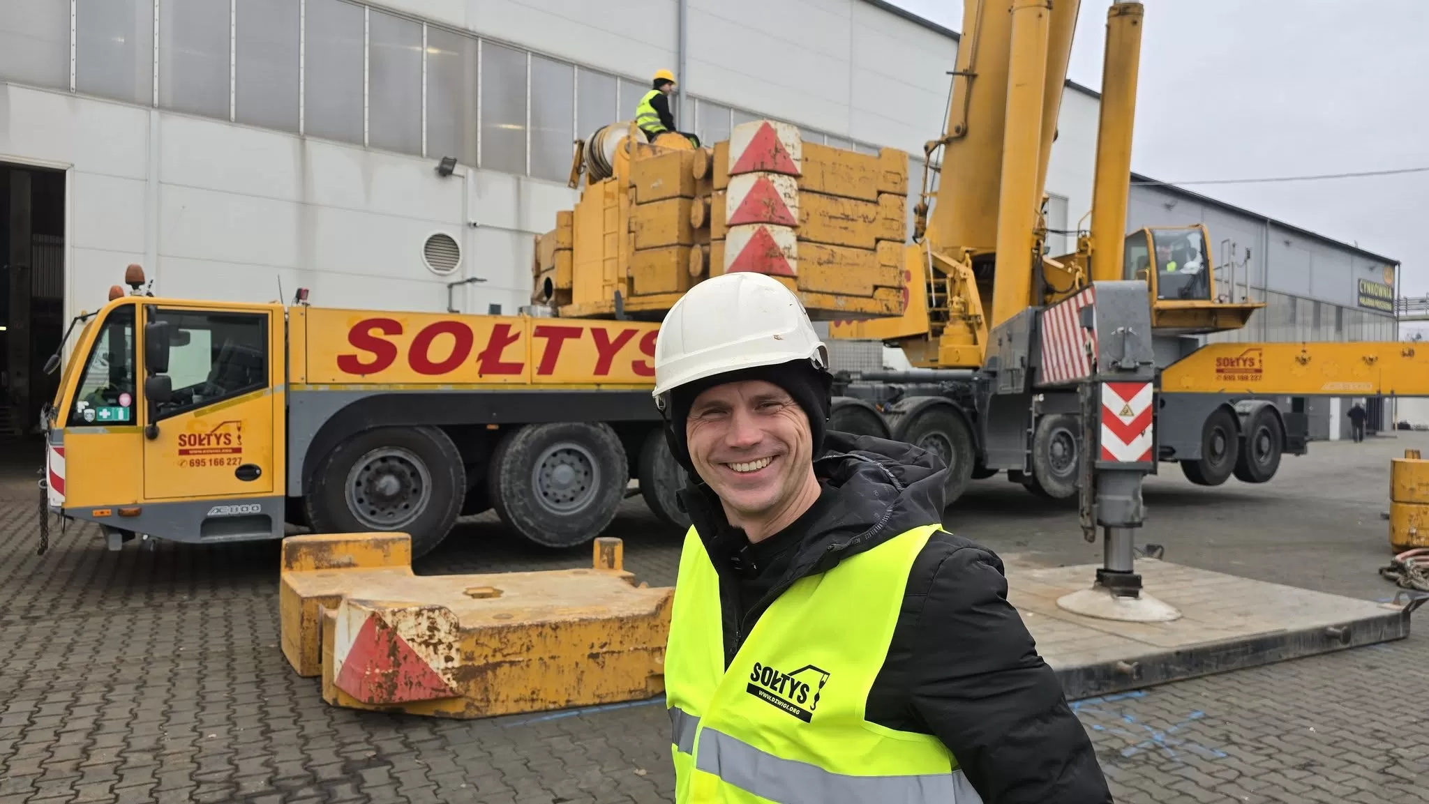 Aleksander Sołtys, właściciel firmy Dźwigi Sołtys Sp. z o.o. stoi na tle żurawia samojezdnego Demag AC 800.